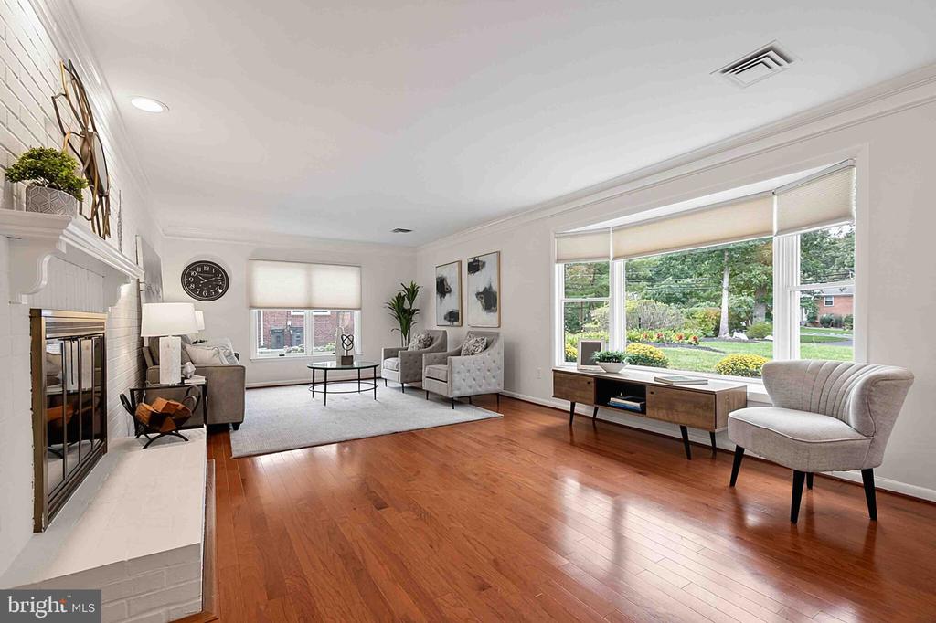 Furnished living room with a white brick fireplace, hardwood floors, and large garden-facing windows.