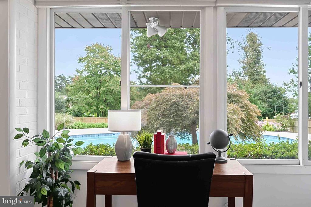Home office with a wooden desk and chair facing large windows overlooking a swimming pool.