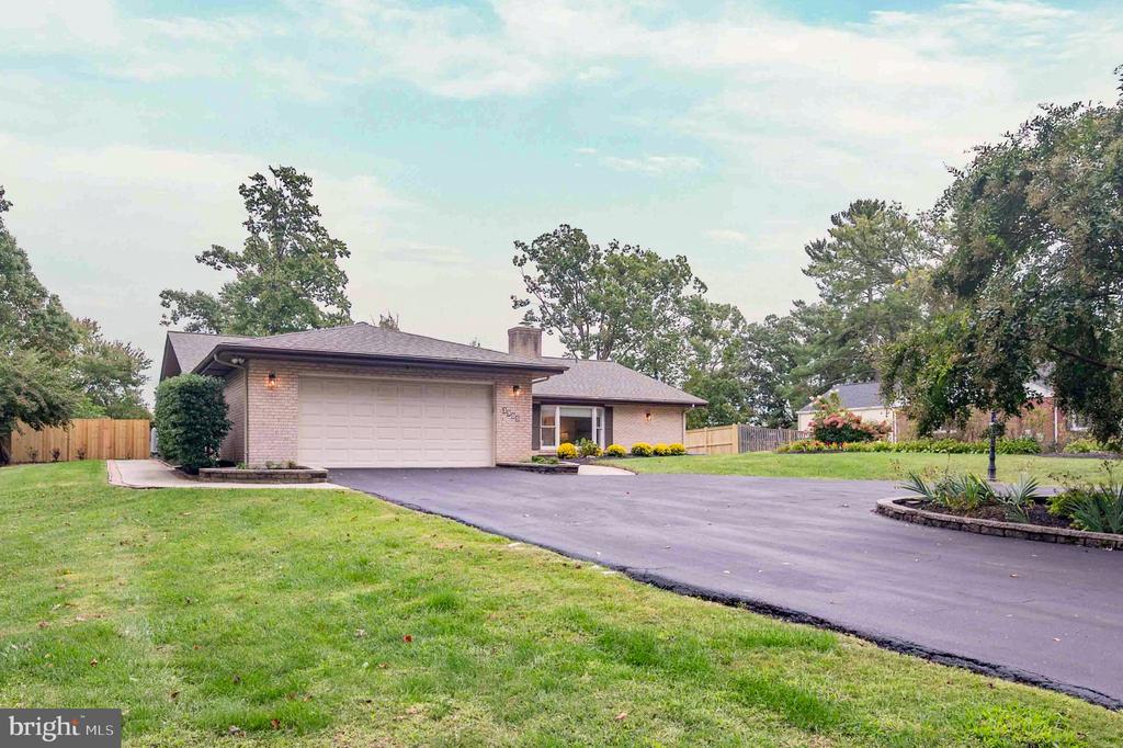 Single-story brick home with an attached garage and broad driveway, framed by lawn and mature trees.