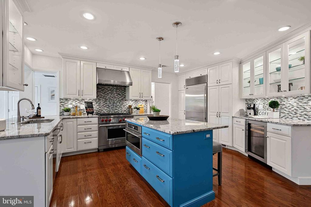 Kitchen with a vivid blue island, white cabinetry, stainless steel appliances, and hardwood floors.