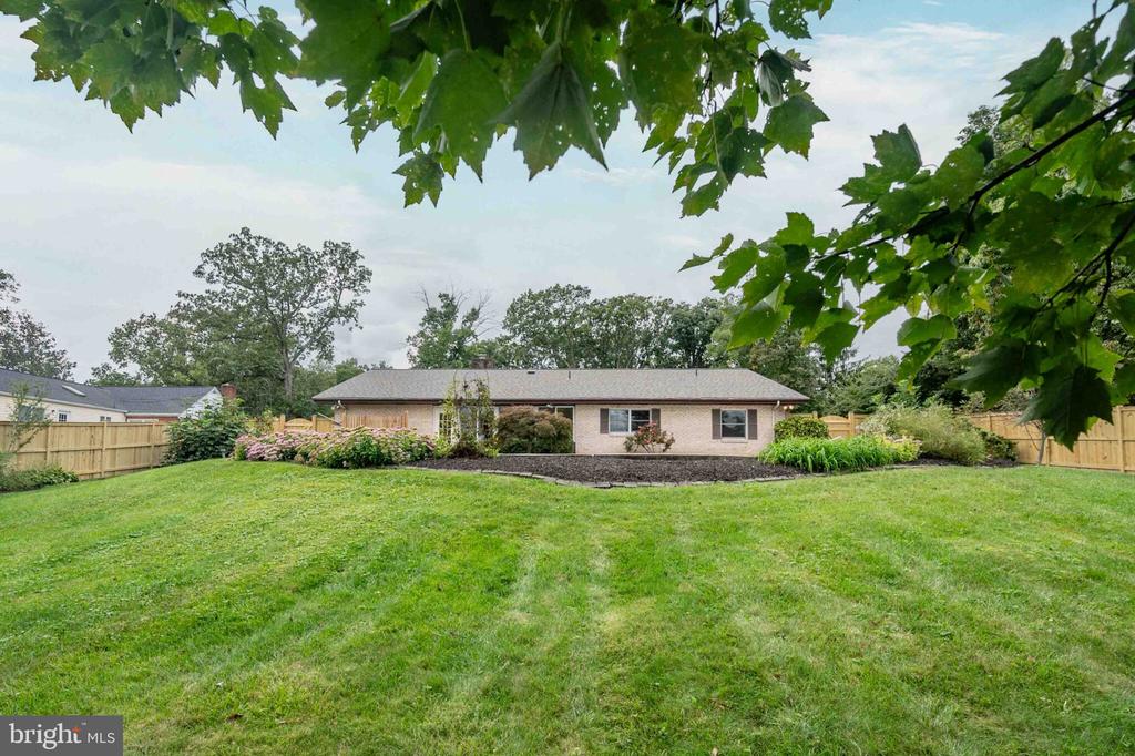 Single-story brick home beyond a broad lawn, with a fenced backyard and leafy branches overhead.