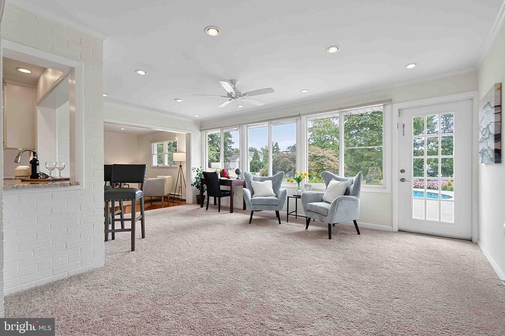 Living room with gray armchairs, broad windows, and a view of trees and the pool.