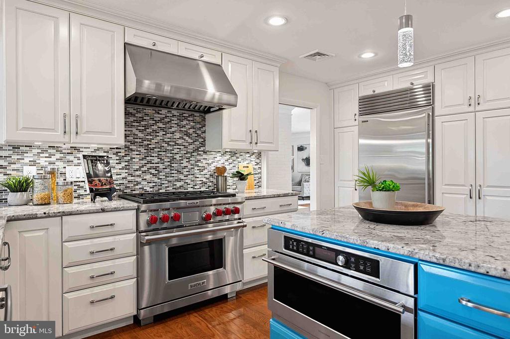 Bright kitchen with a stainless steel Wolf range, mosaic backsplash, and stone island with blue cabinetry.