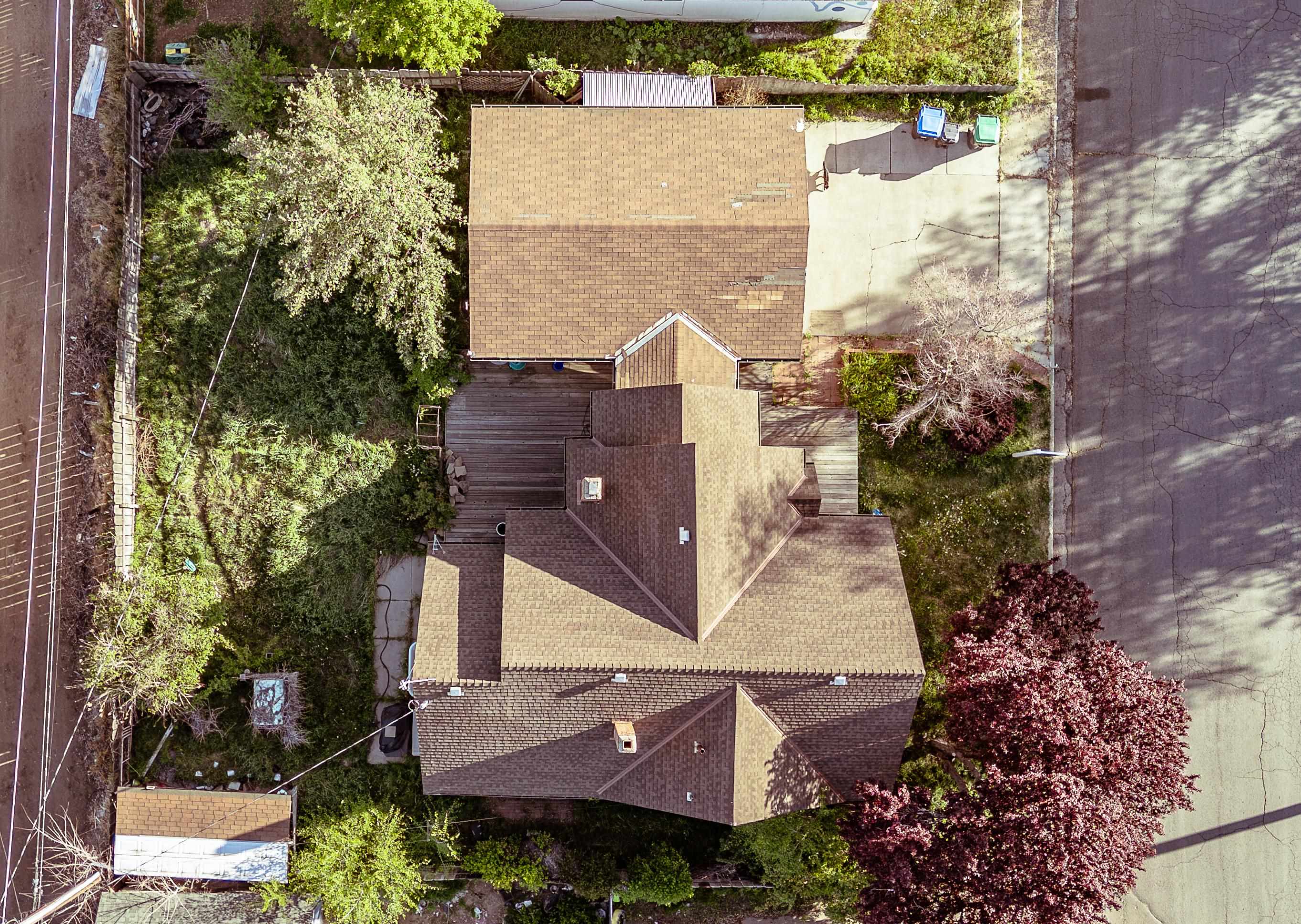 Aerial view of a house with a wooden deck, leafy yard, and paved driveway.