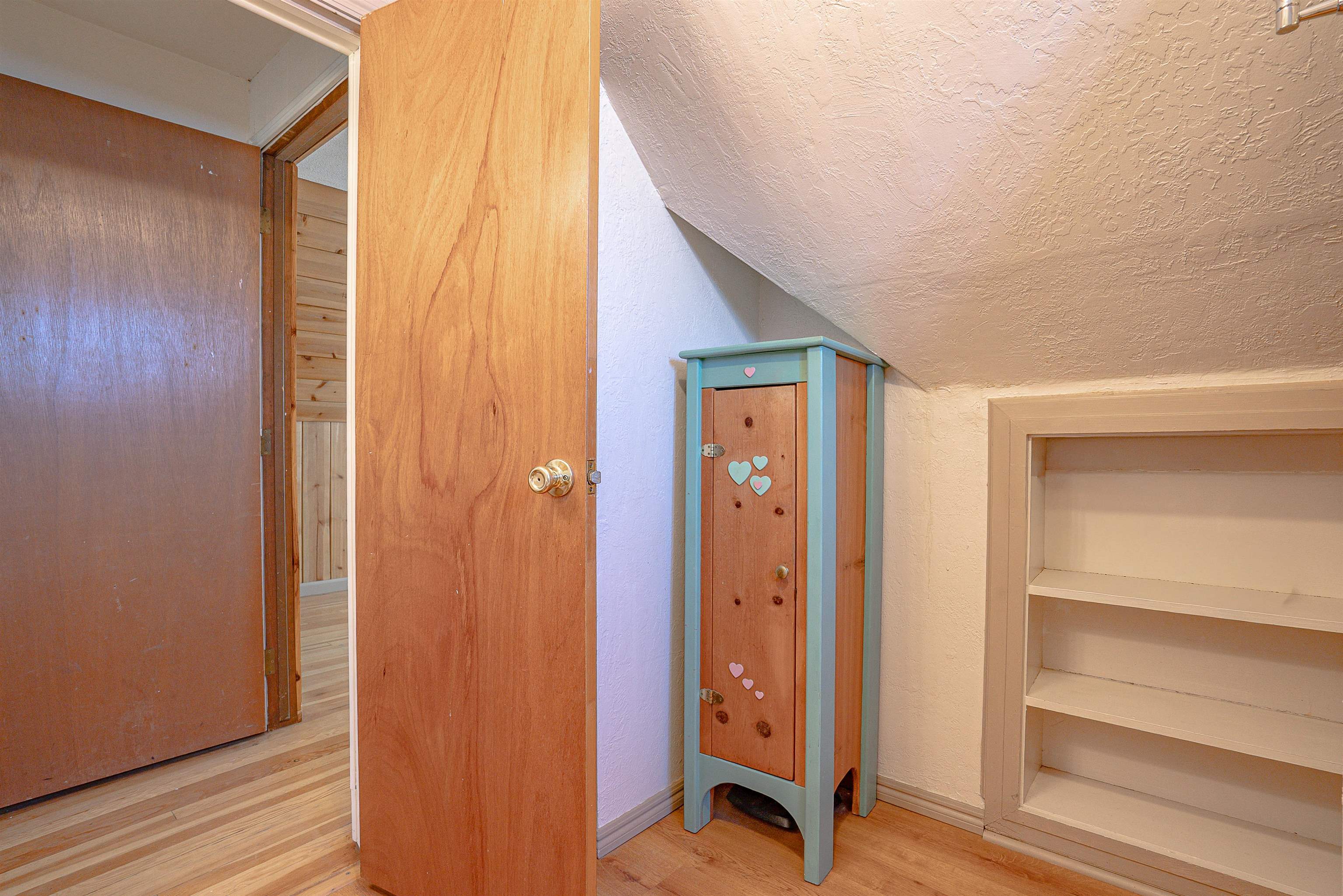 Small room under a sloped ceiling with built-in shelves and a teal cabinet decorated with hearts.