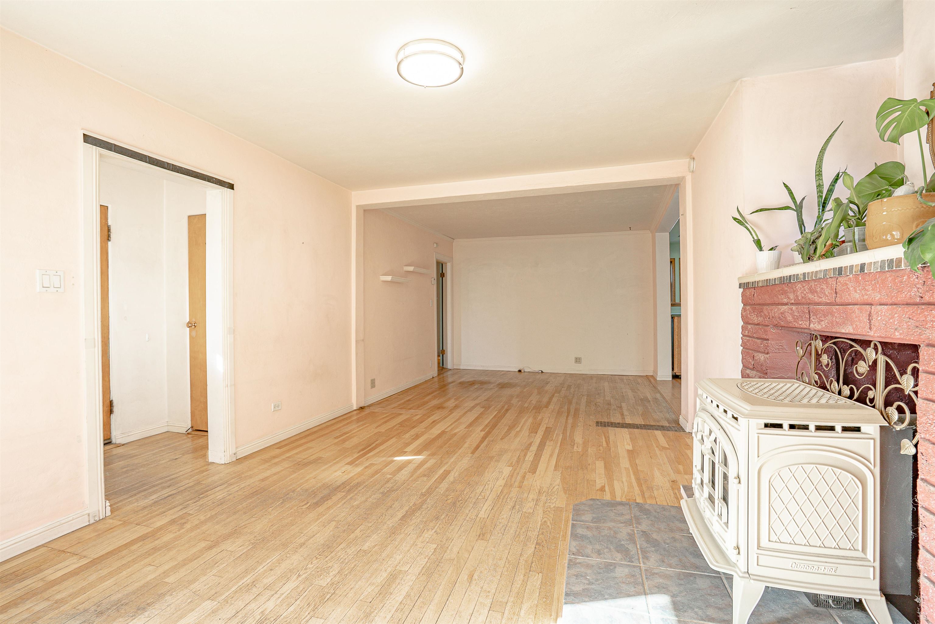 Vacant living room with hardwood floors, a brick fireplace, and a white freestanding stove.