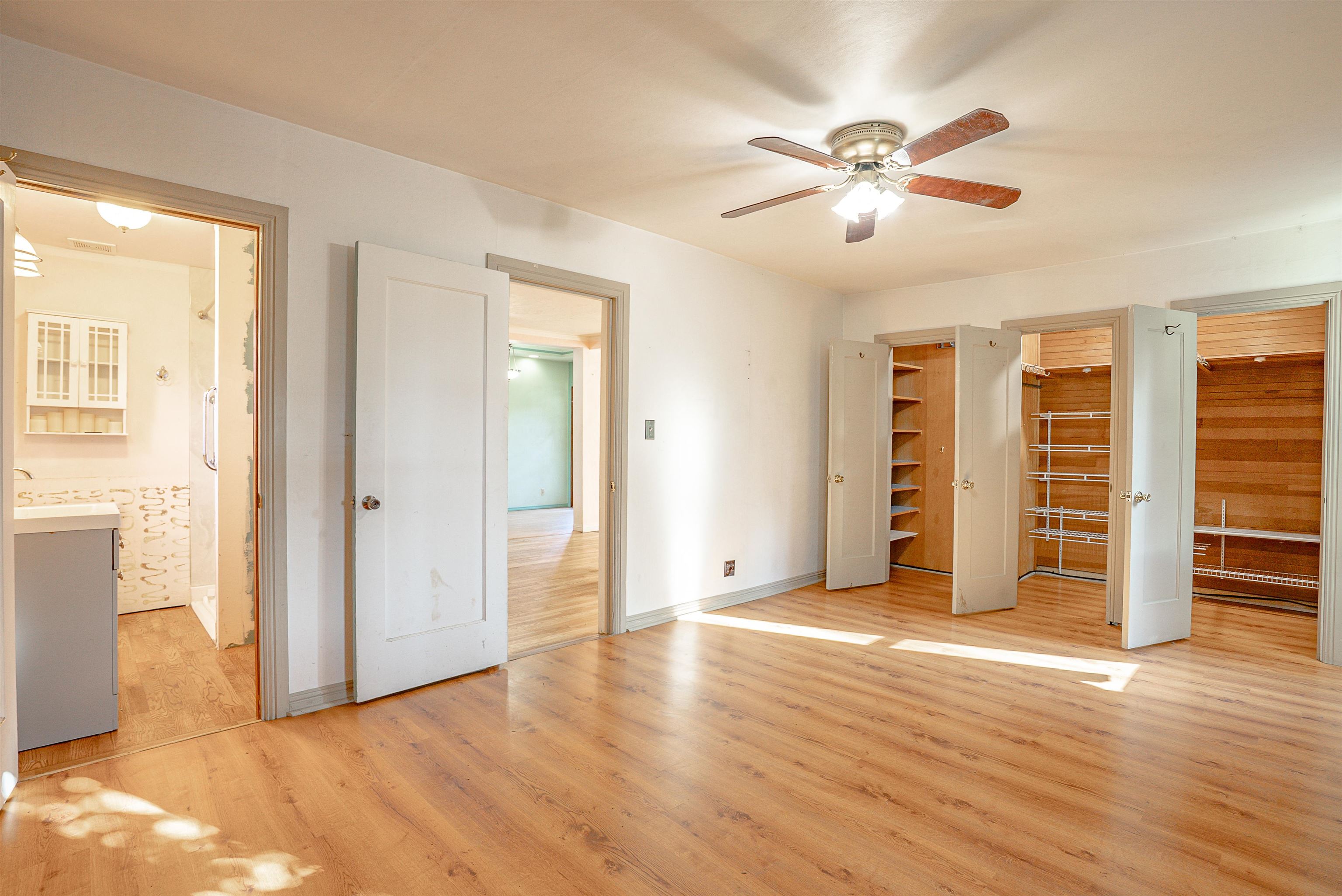 Vacant bedroom with wood floors, a ceiling fan, and multiple open built-in closets.