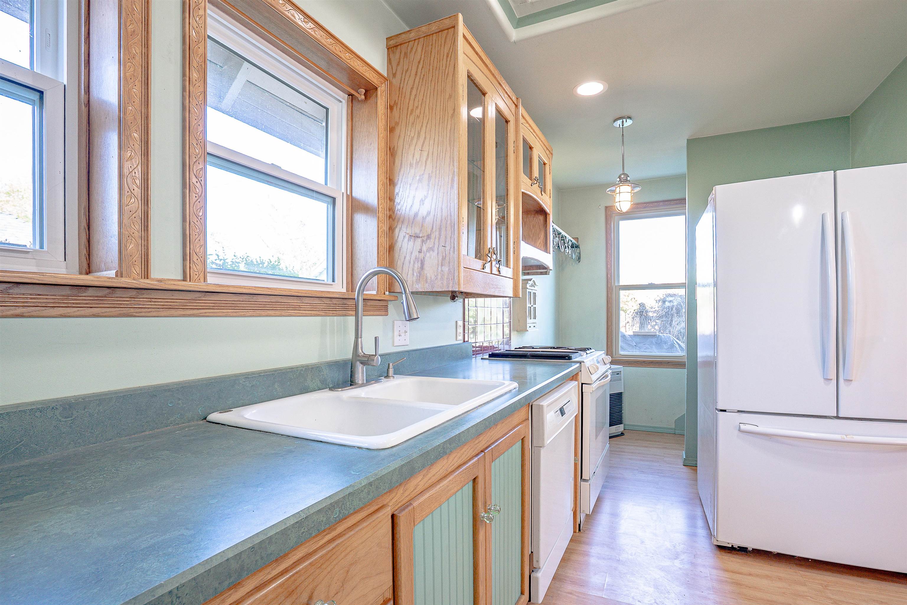 Kitchen with carved wood cabinets, blue-green counters, a double sink, and white appliances.