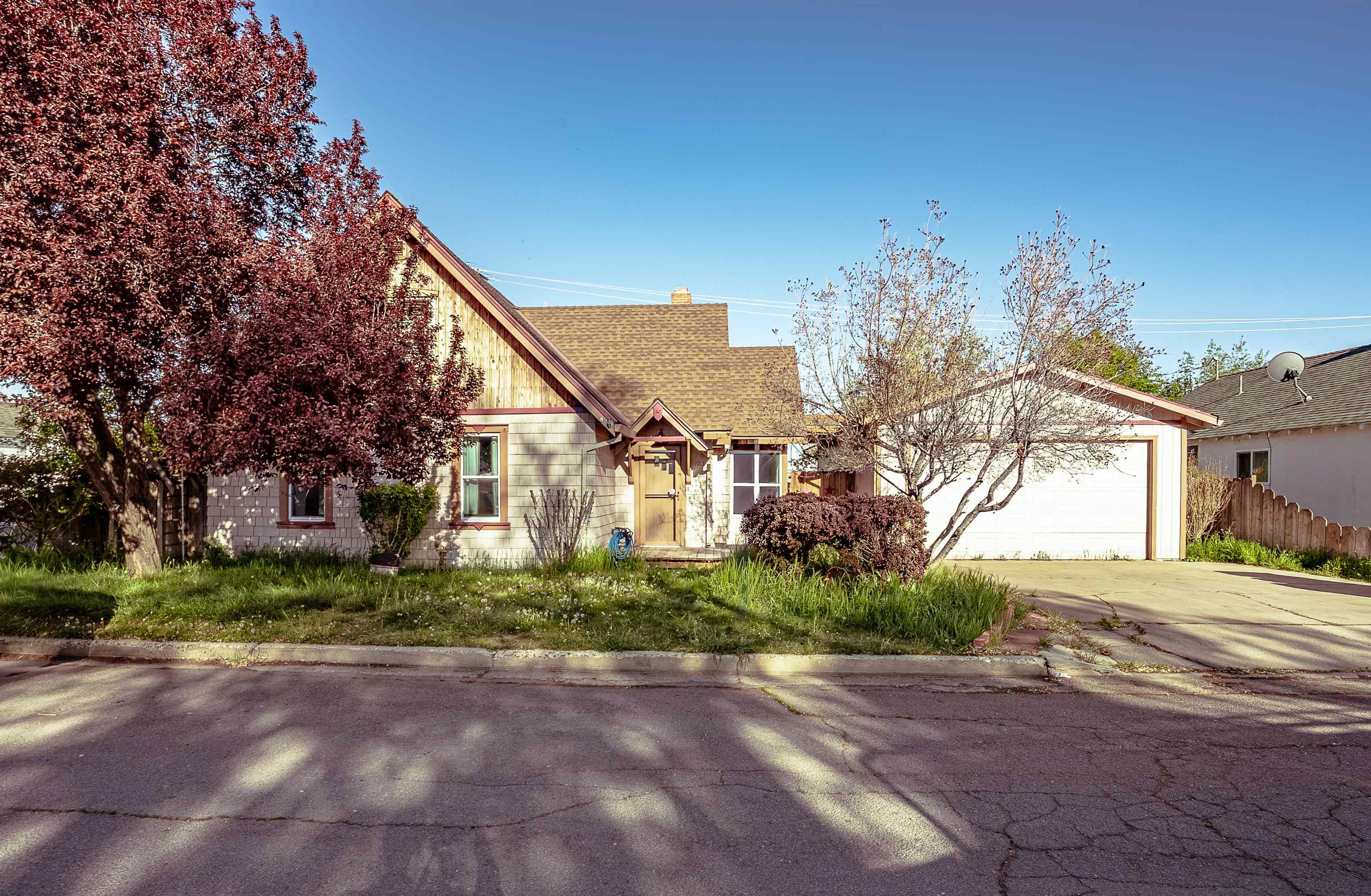 House with a steep gabled roof, attached garage, and mature trees in the front yard.