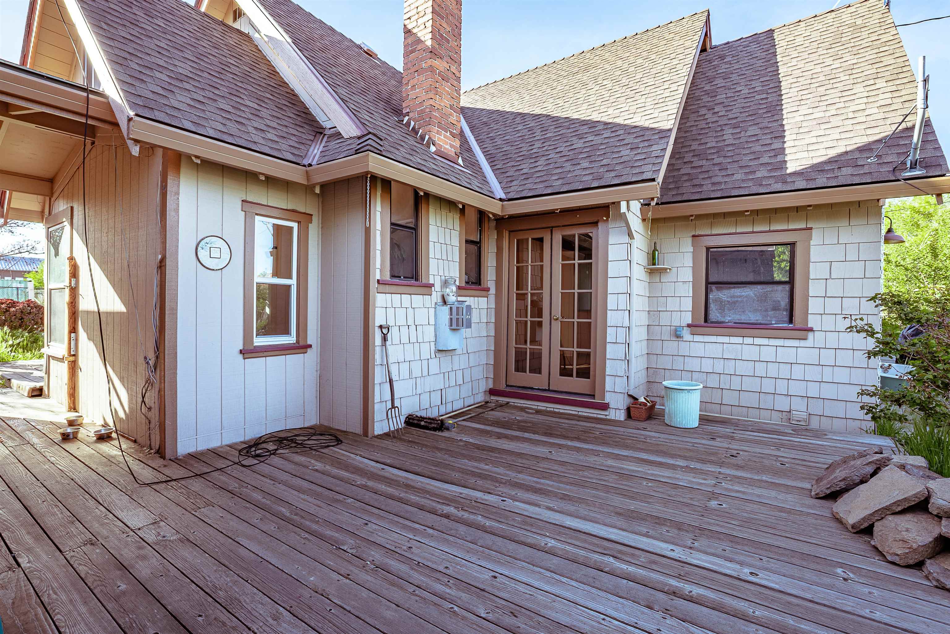 House exterior with a large wooden deck, glass-paneled double doors, and a brick chimney.