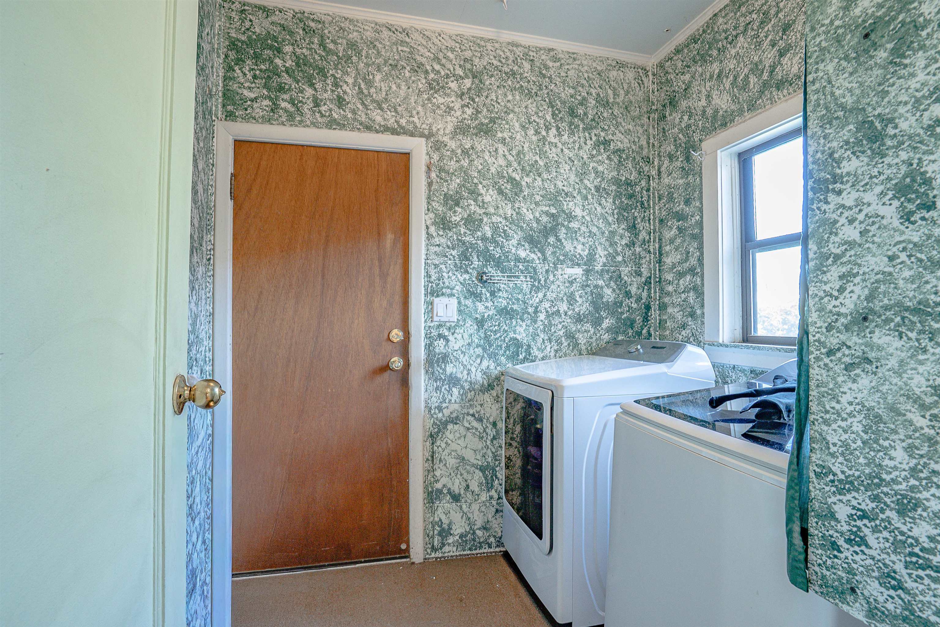 Laundry room with white washer and dryer, patterned wallpaper, and a brown door.
