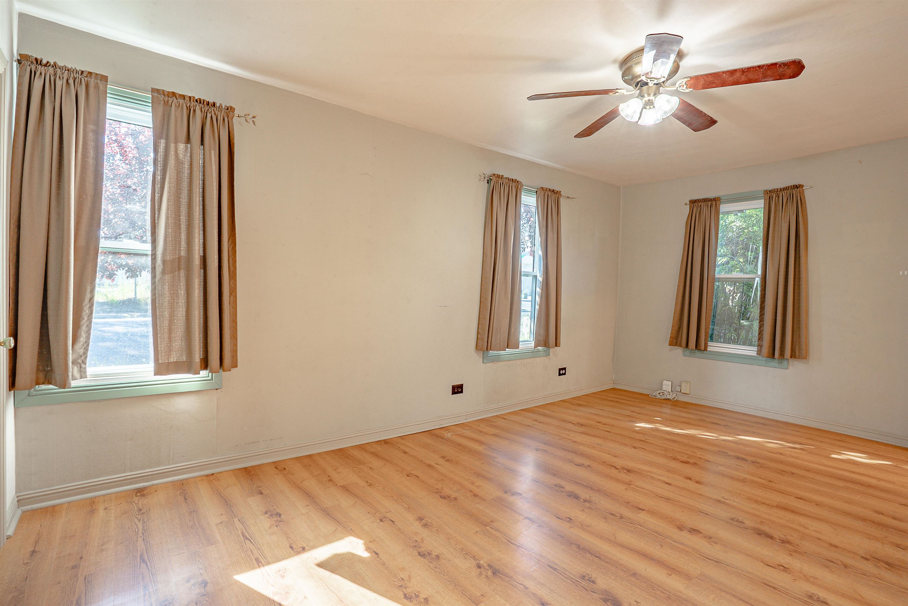 Empty room with wood floors, three curtained windows, and a ceiling fan.