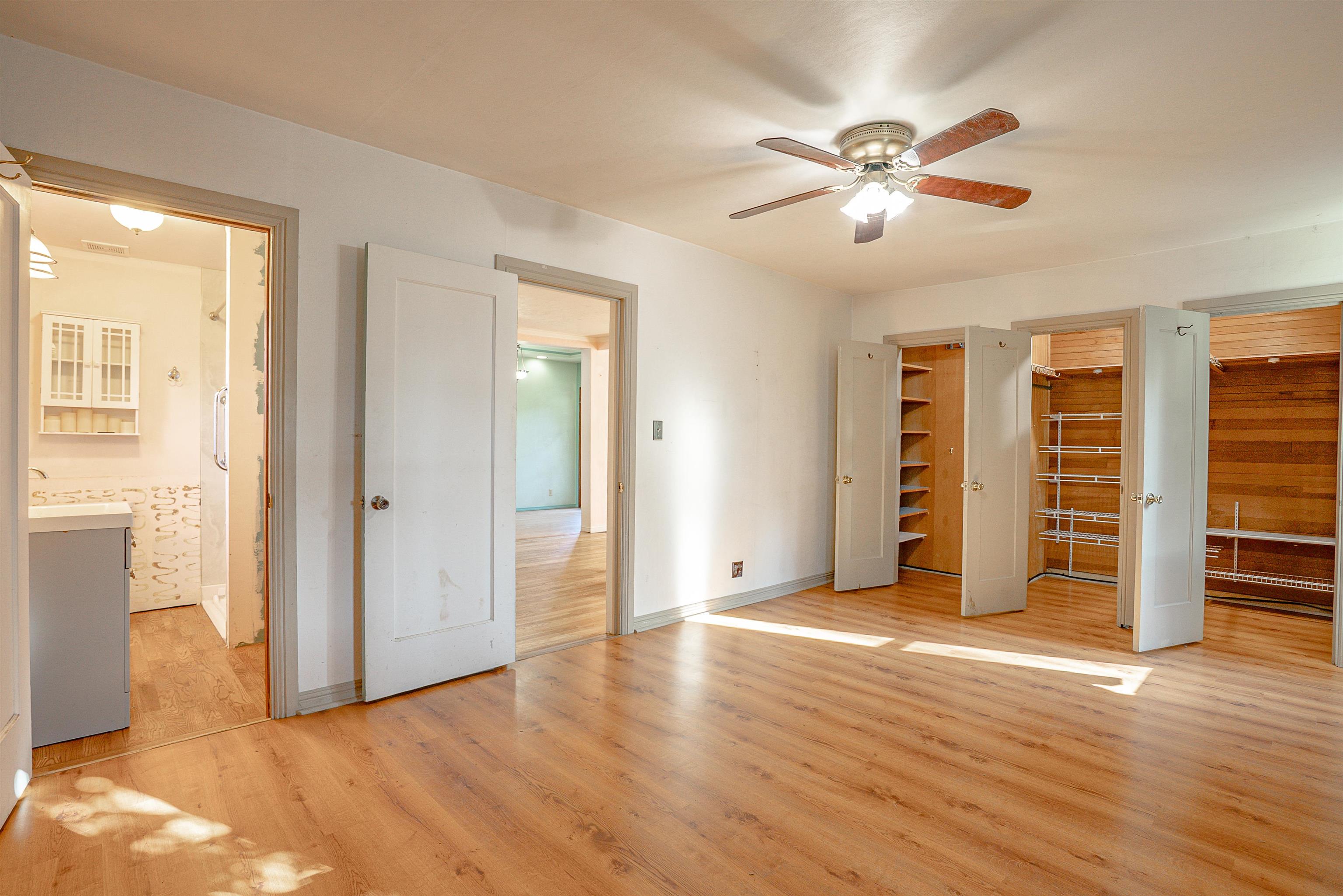 Vacant bedroom with wood floors, a ceiling fan, and several open closets.