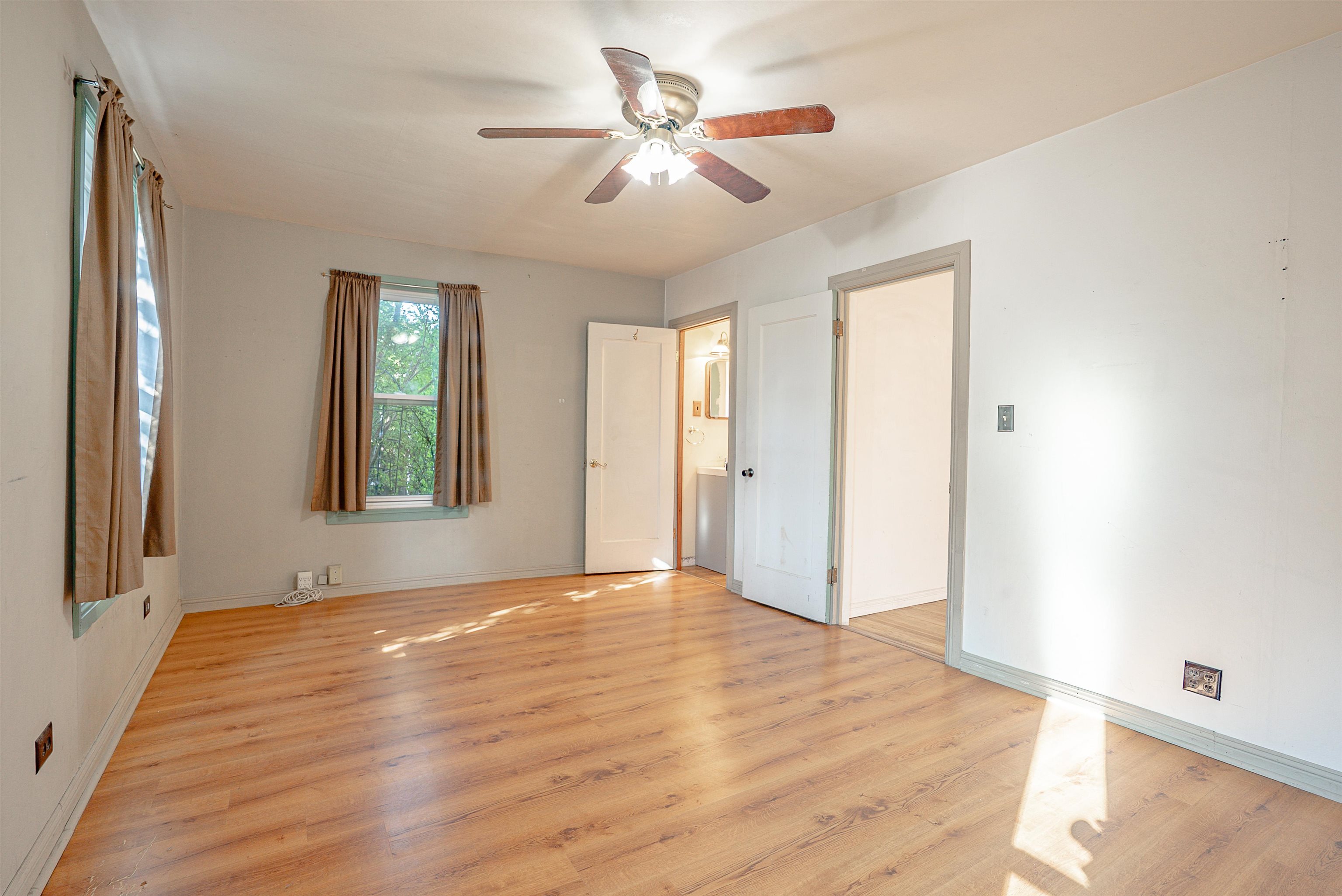 Empty bedroom with wood floors, curtained windows, and a ceiling fan.