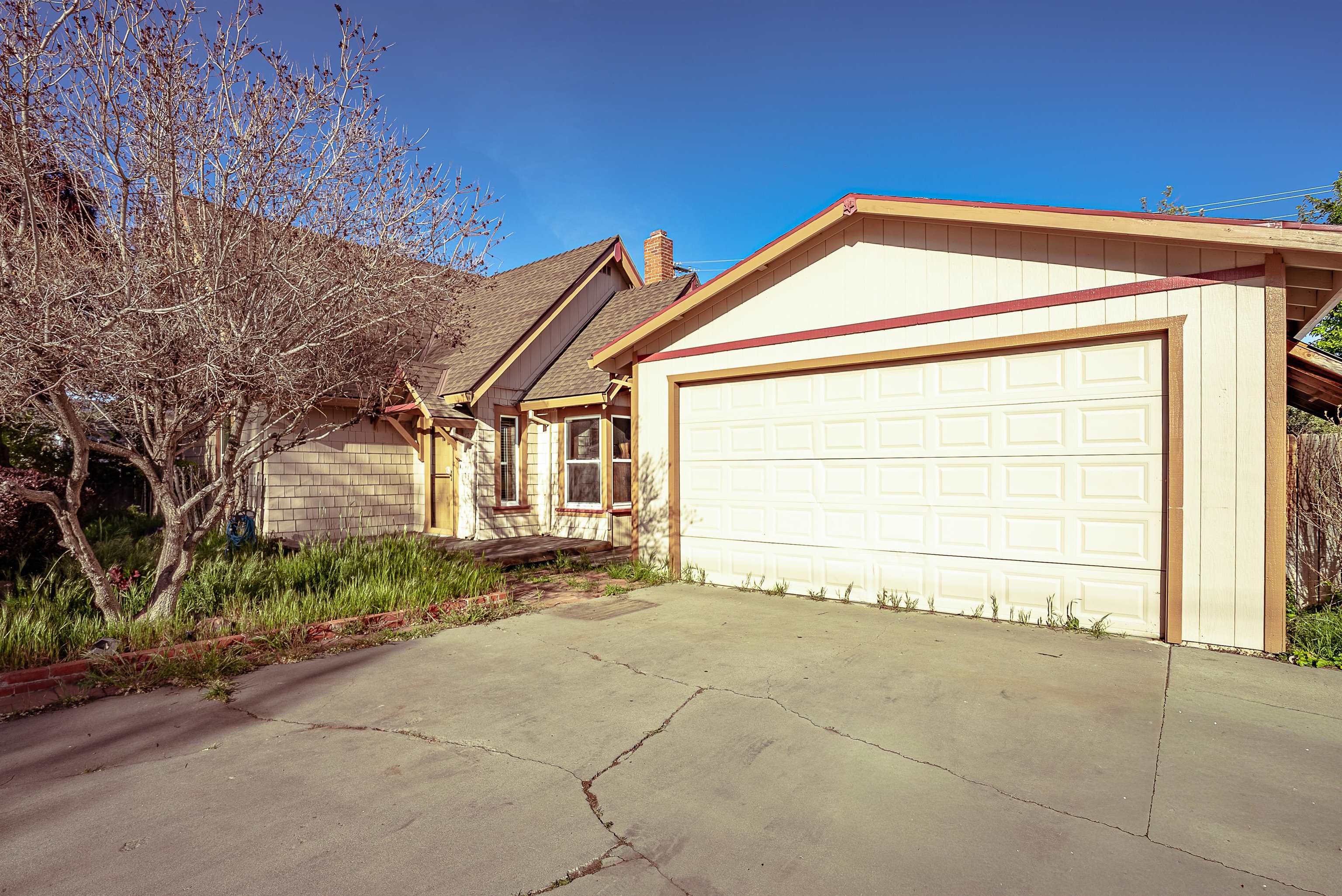 House exterior with a large white garage door, cracked driveway, and leafless tree.