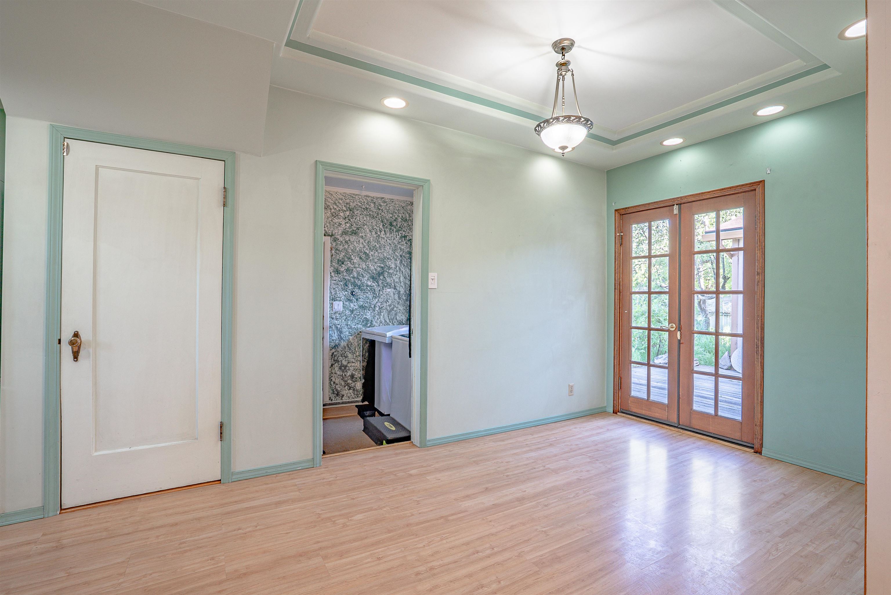 Empty room with a tray ceiling, light wood flooring, and French doors opening to a deck.