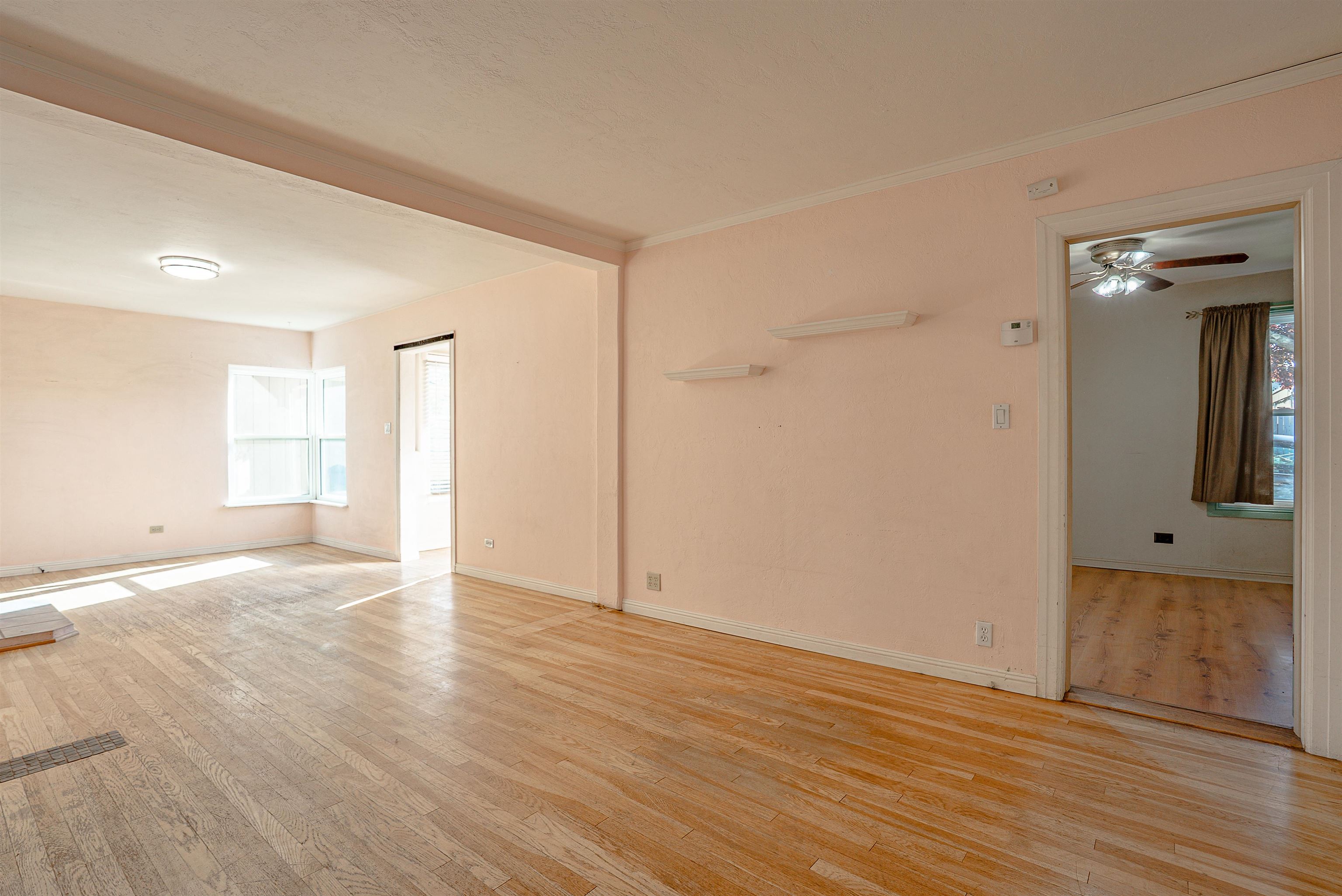 Empty living room with peach walls, worn hardwood floors, and a corner window.