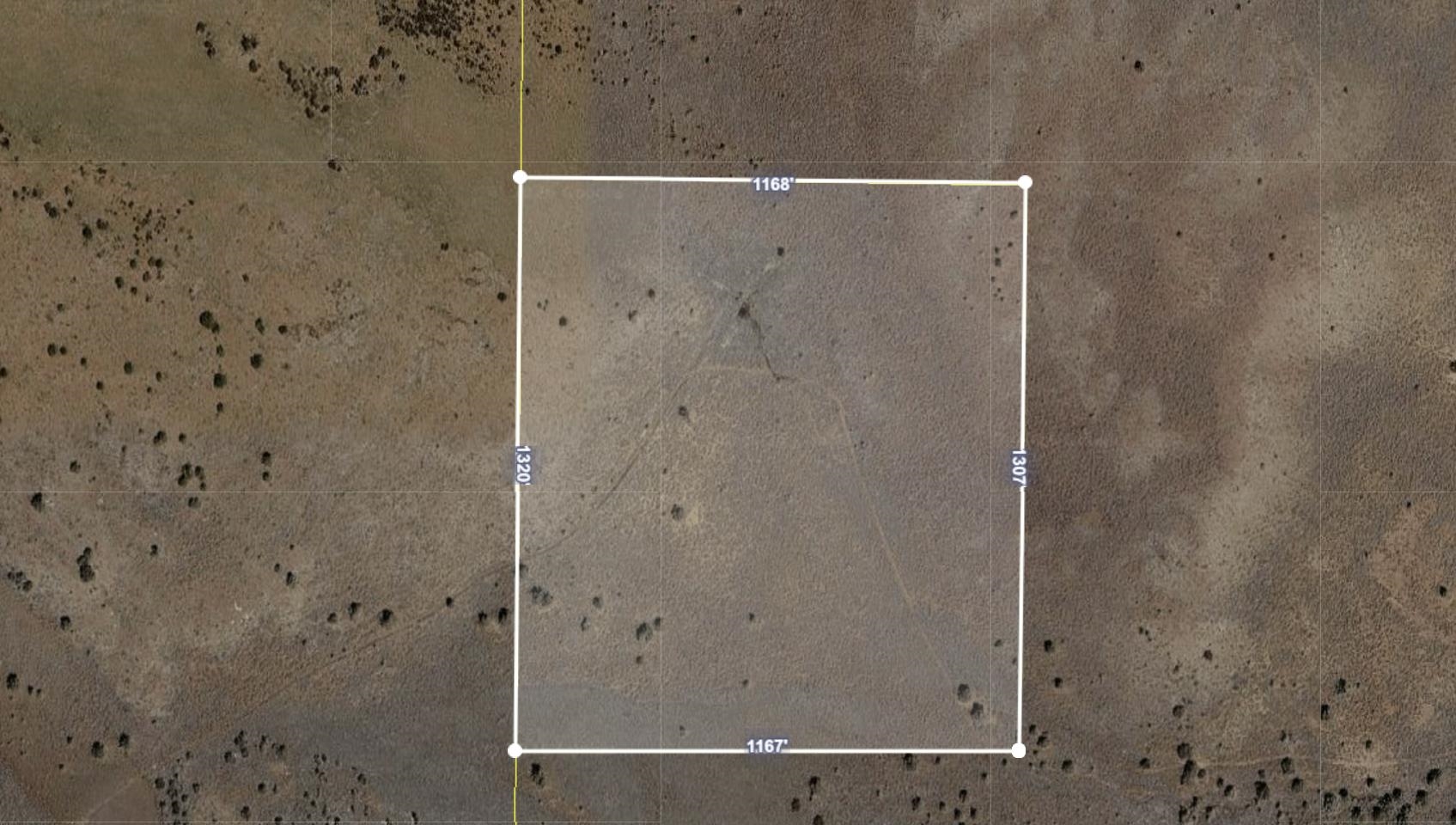 Aerial view of undeveloped land outlined with measurements, surrounded by dry terrain and sparse shrubs.
