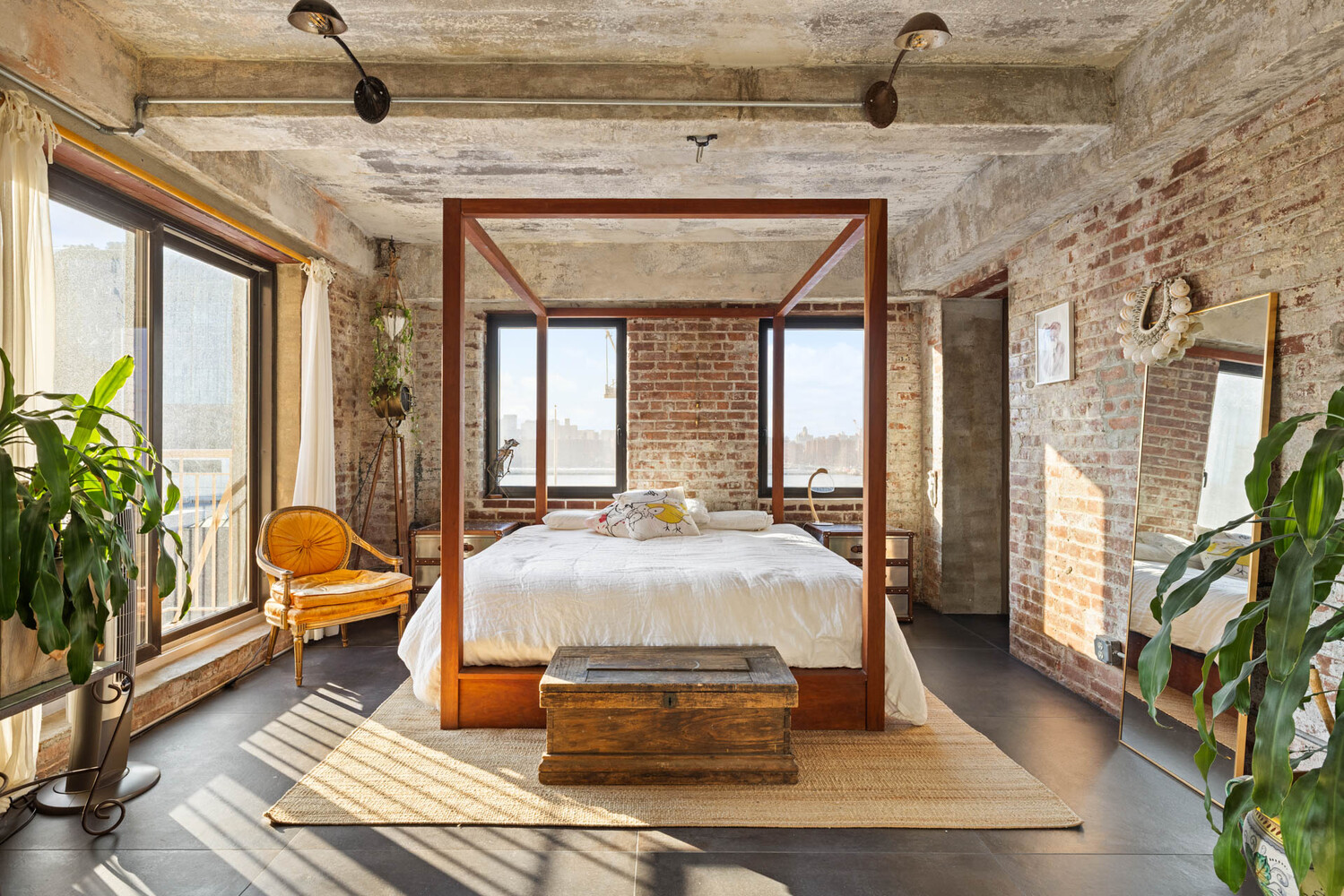 Bedroom with exposed brick, a wooden four-poster bed, and sunlight streaming through balcony doors.