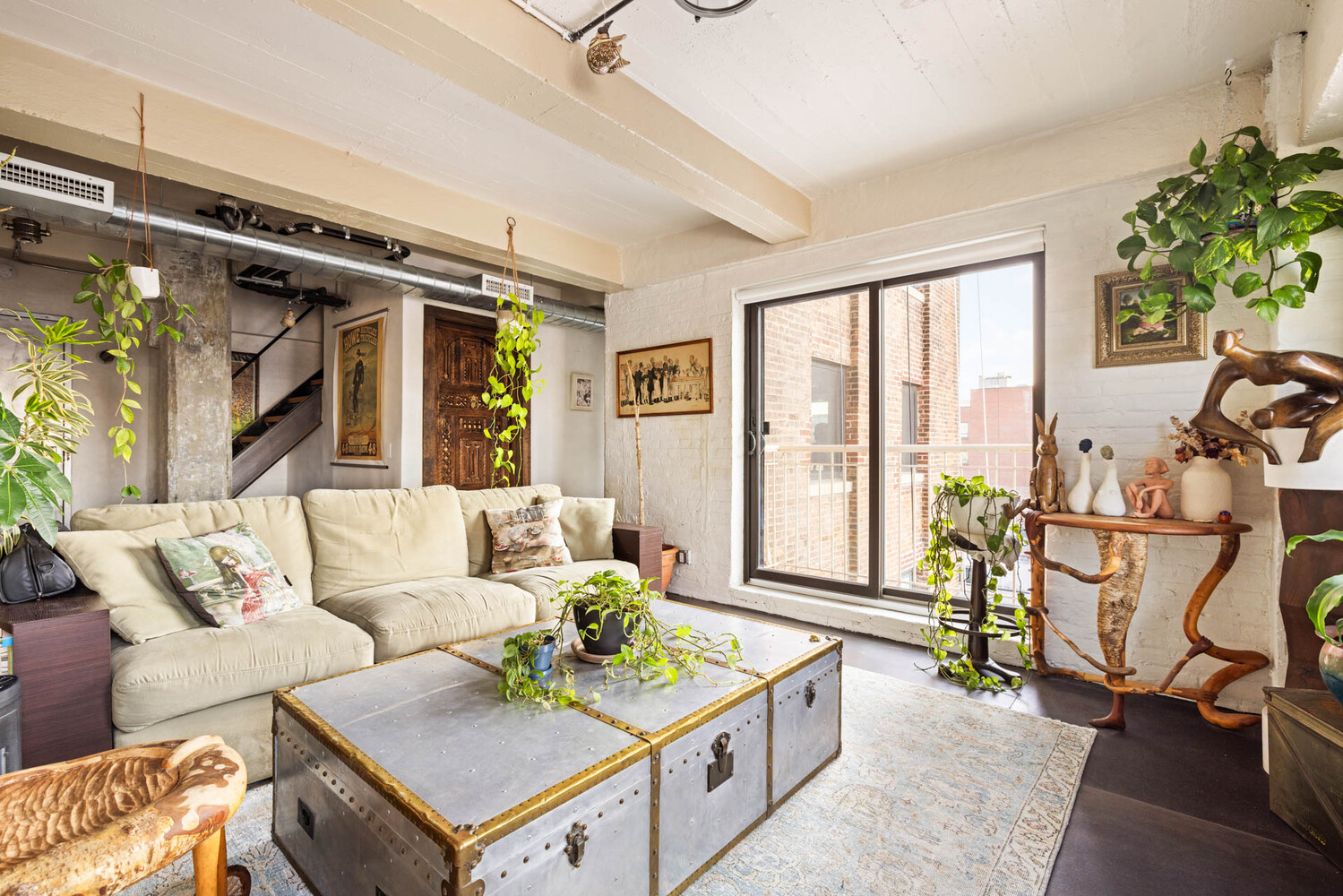 Living room with exposed ductwork, a cream sectional, metal trunk coffee table, and balcony doors.