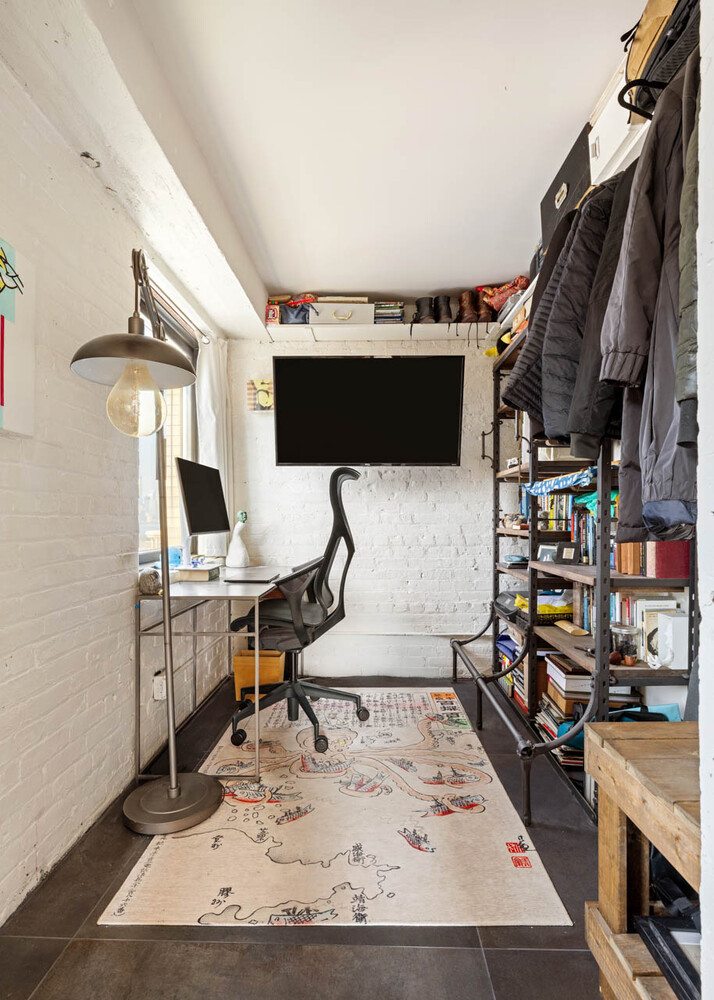 Compact home office with white brick walls, a desk, wall-mounted television, and map-patterned rug.