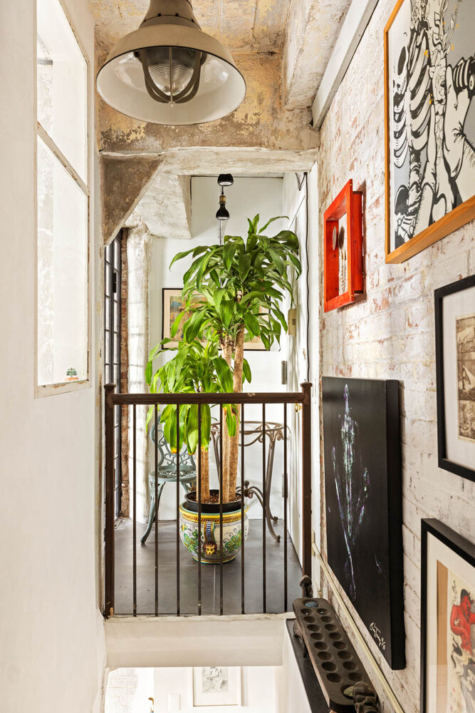 Loft-style apartment landing with exposed brick, framed artwork, a metal railing, and a tall potted plant.