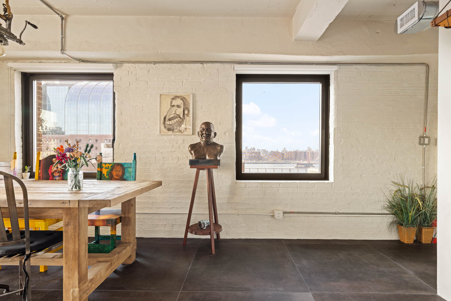 Furnished dining area with exposed white brick, colorful artwork, and windows overlooking the skyline and water.