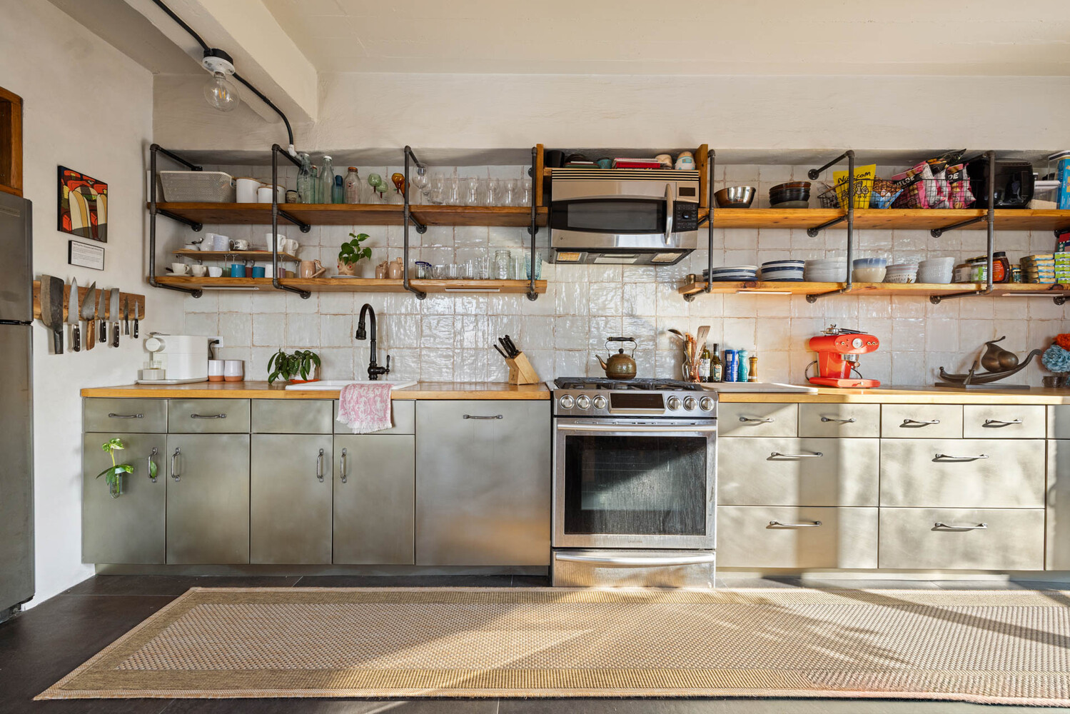 Kitchen with stainless-steel cabinets, open shelving, and a tiled backsplash.