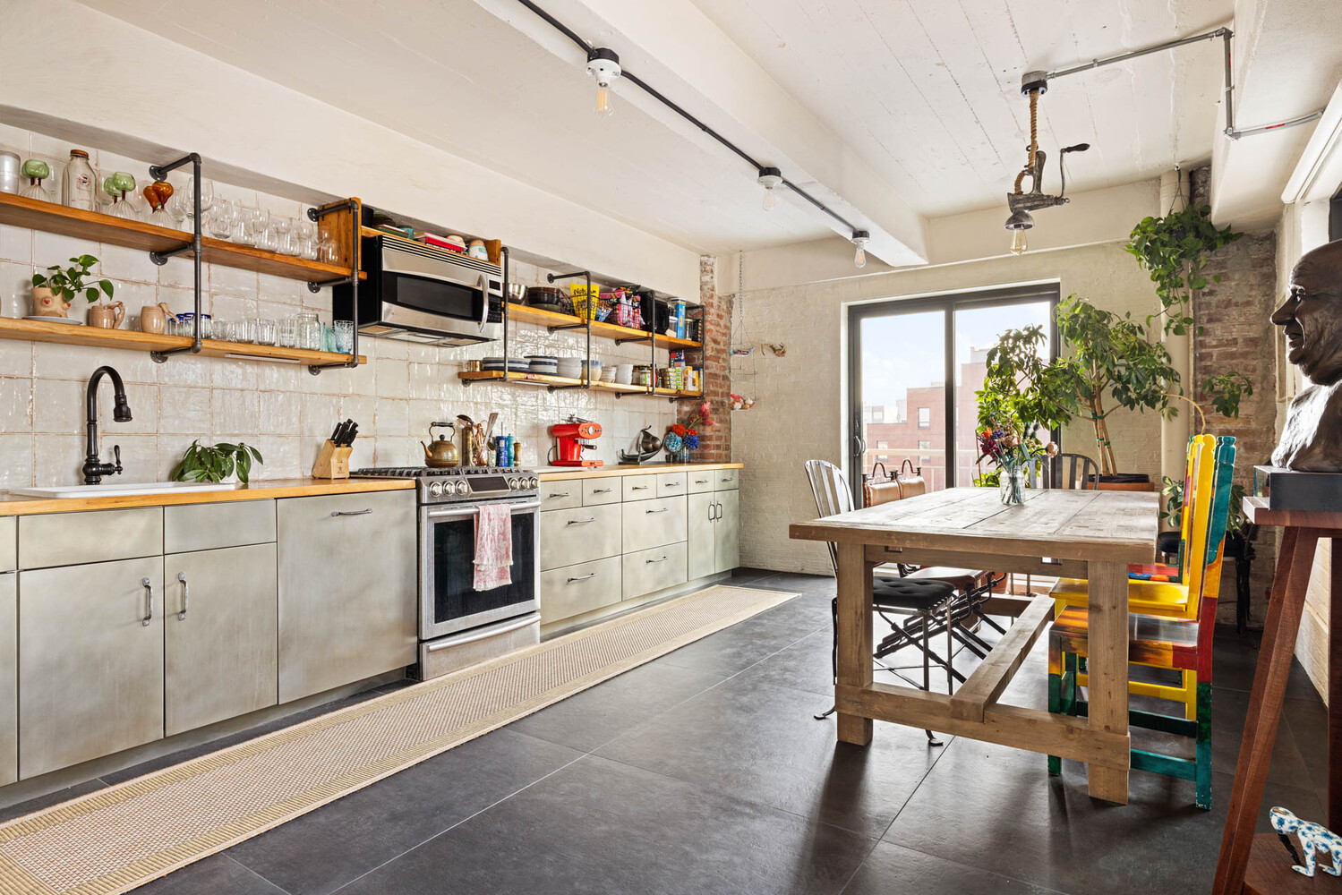 Industrial-style kitchen and dining area with open shelving, stainless appliances, and colorful chairs.