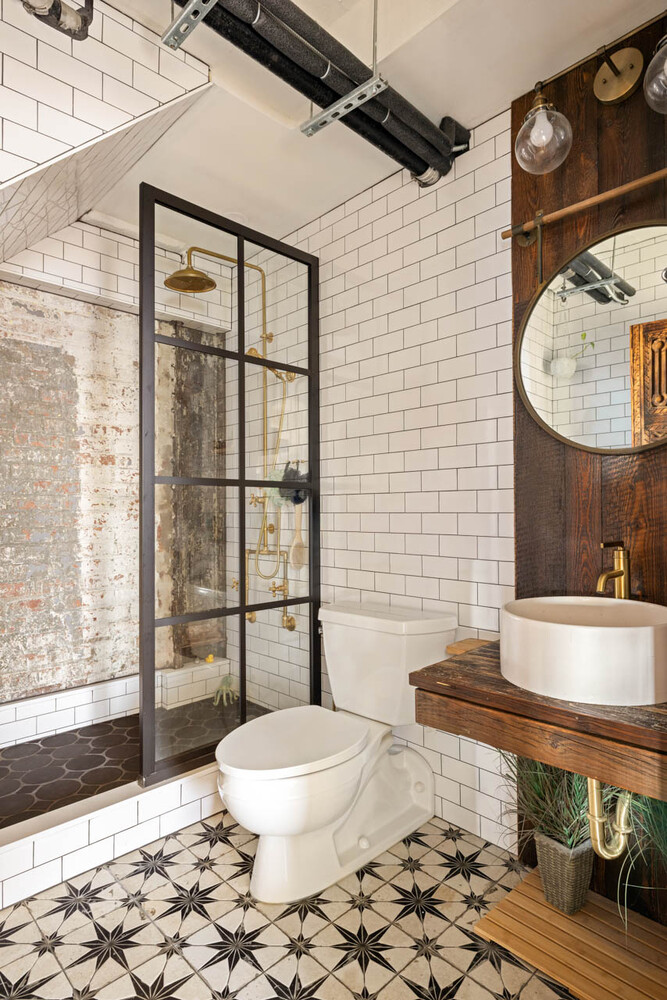 Bathroom with a black-framed glass shower, exposed brick, and patterned tile floor.