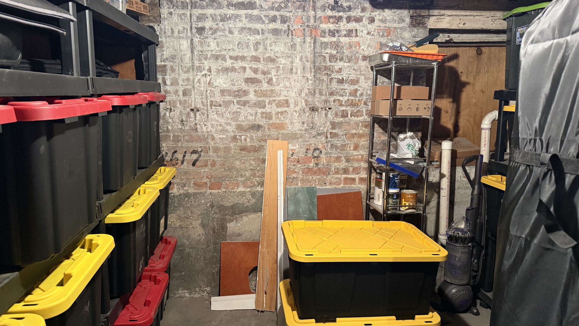 Basement storage area with exposed brick walls, stacked bins, and a metal utility rack.