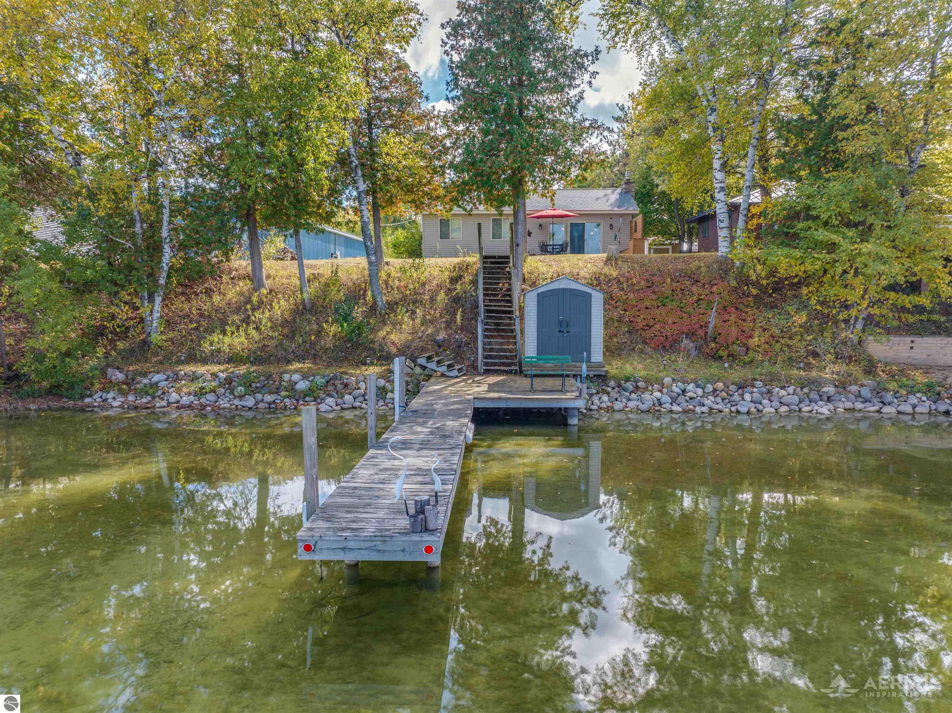 Lakeside home with a long dock, rocky shore, hillside stairs, and small shed.