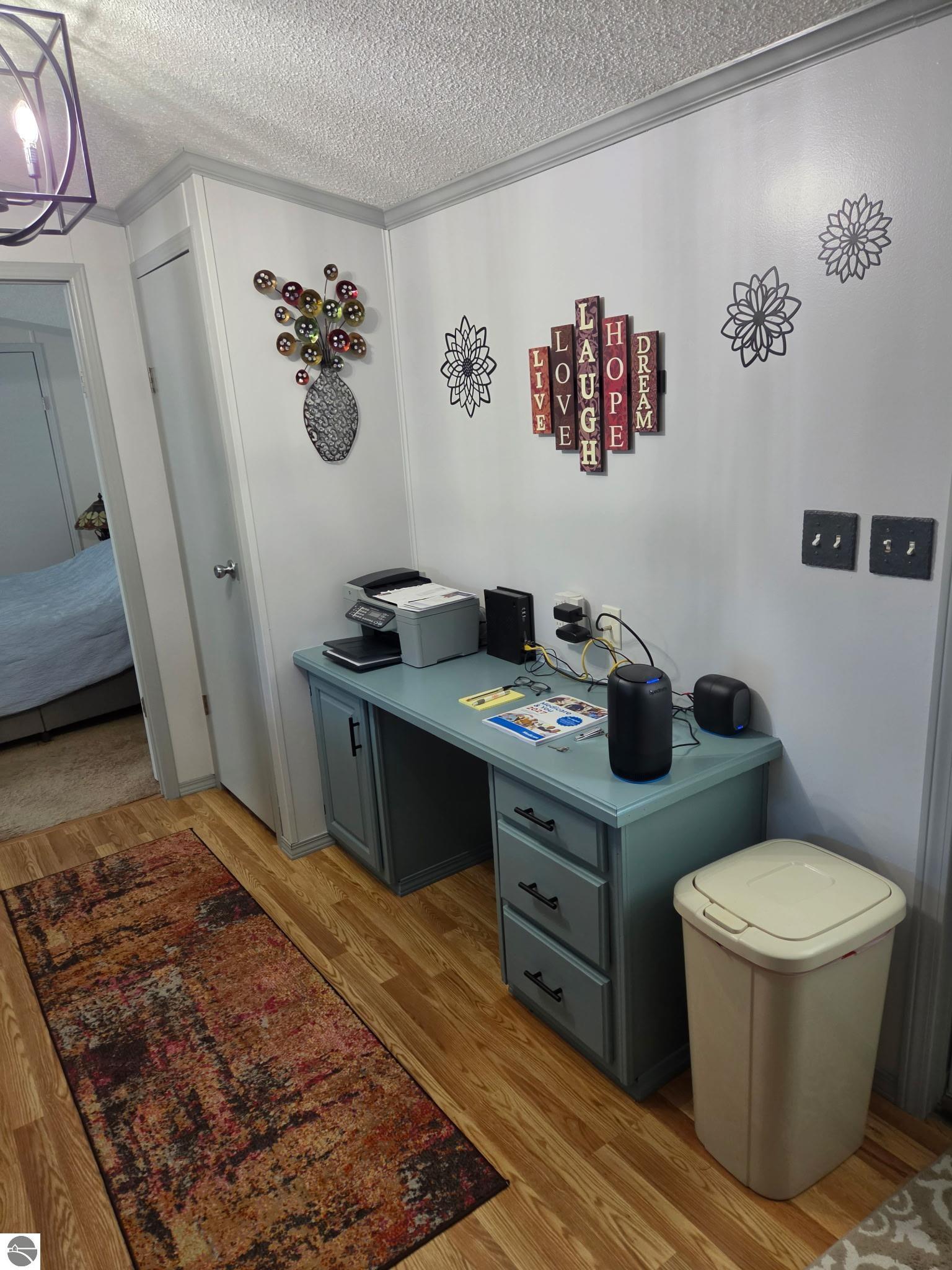Home office with a teal desk, printer, decorative wall art, and hardwood floors.