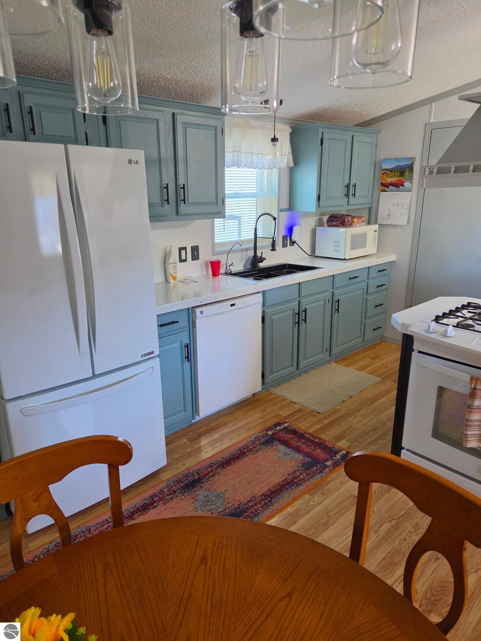 Kitchen with blue-green cabinets, white appliances, and a round wooden dining table in the foreground.