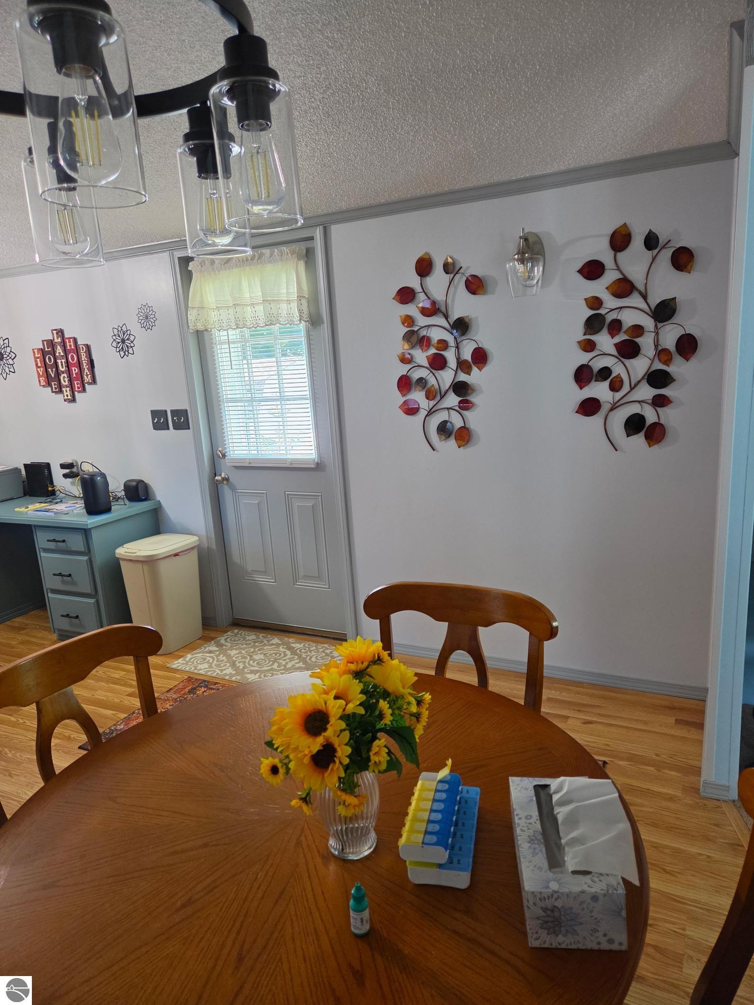 Dining room with a wooden table, sunflower centerpiece, glass pendant lights, and decorative metal leaves.