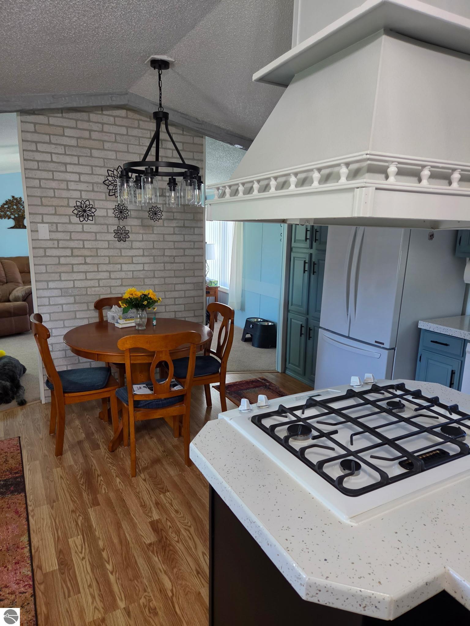 Kitchen and dining area with a gas cooktop peninsula, blue cabinets, and a brick accent wall.