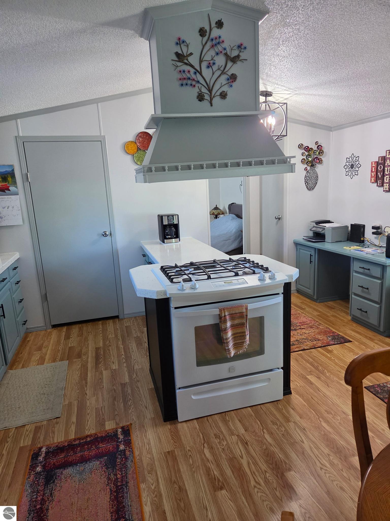 Kitchen with a white island range, oversized decorative hood, and blue-gray cabinetry.