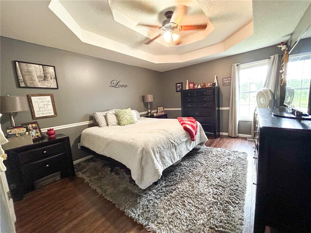 Bedroom with a white bed, dark dressers, and a tray ceiling with a ceiling fan.