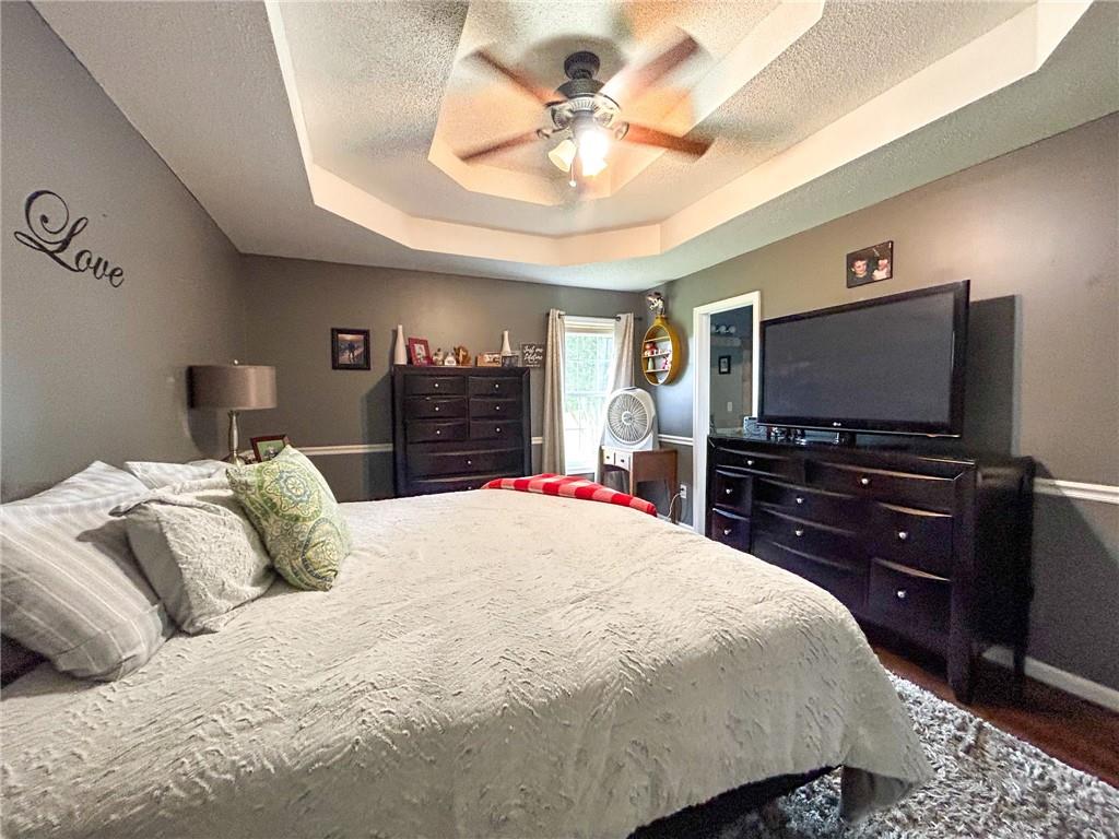 Furnished bedroom with a large bed, tray ceiling, ceiling fan, and television.