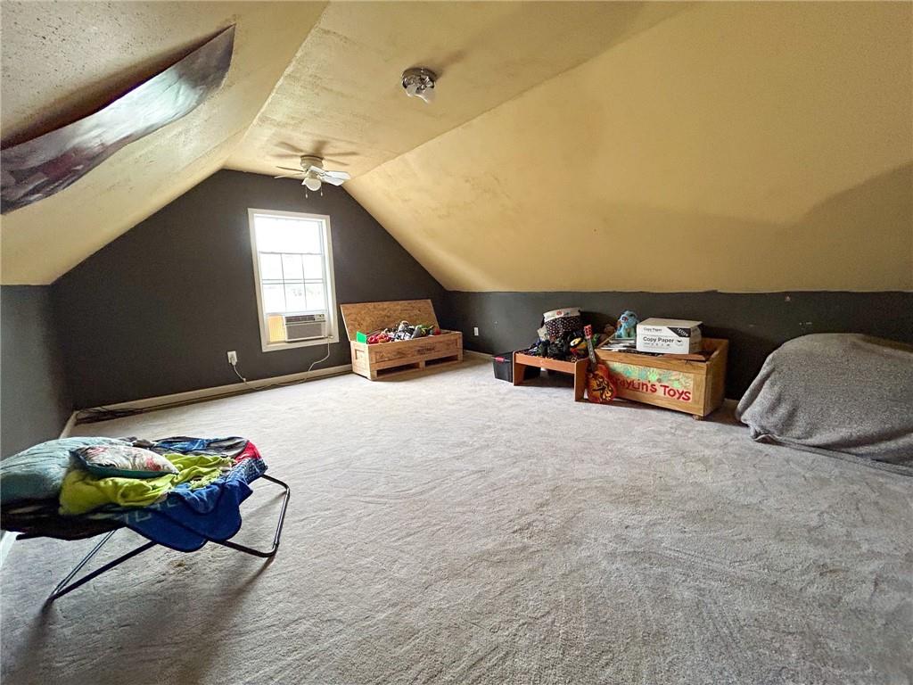 Carpeted attic room with sloped ceilings, a window air conditioner, ceiling fan, and toy storage.