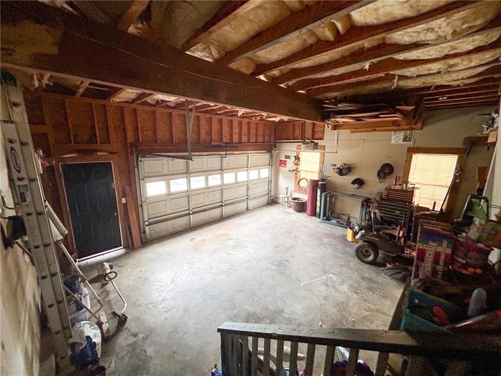 Garage with a concrete floor, large sectional door, exposed rafters, and tools and storage along the walls.