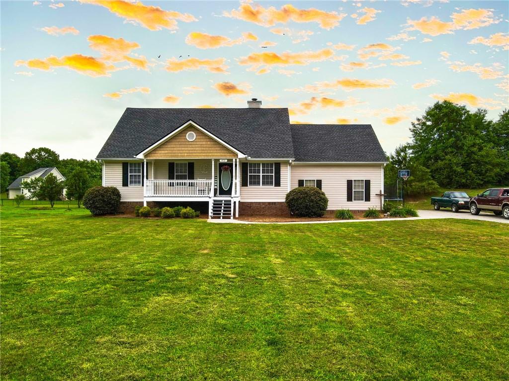 Single-story beige home with a covered porch and broad green lawn beneath a colorful evening sky.