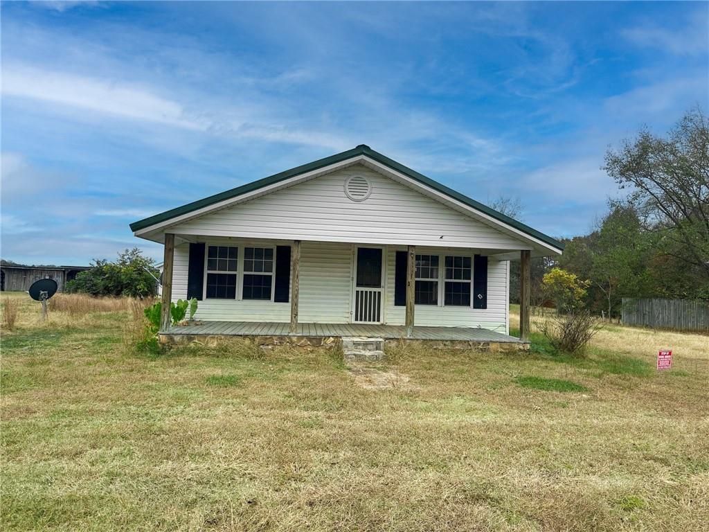 White single-story house with a covered front porch and green gabled roof in a grassy yard.