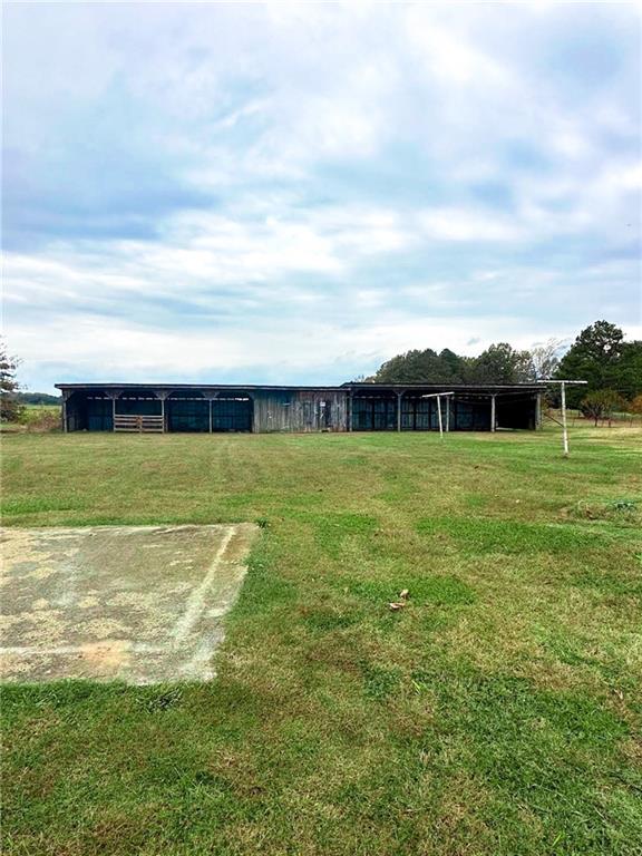 Long weathered outbuilding with open-sided sections and a metal roof across a grassy yard.