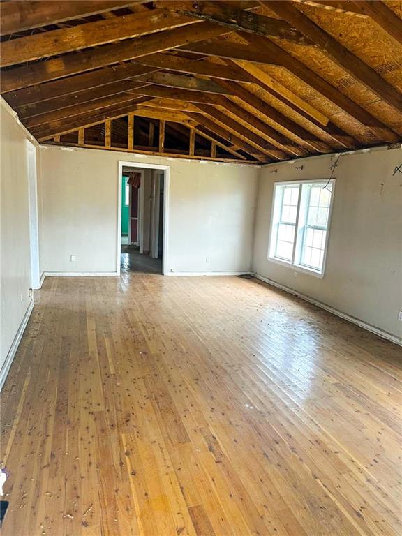 Vacant room with exposed timber rafters, worn wood floors, and a large window.