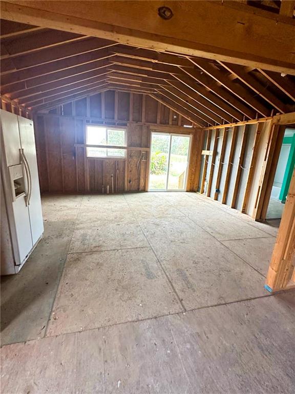 Unfinished room with exposed timber framing, a bare plywood floor, and windows beside a glass door.
