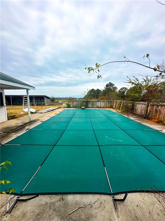 Backyard swimming pool covered with a teal safety cover beside a fenced yard and covered patio.