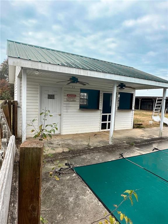 White-sided building with a green metal roof beside a covered swimming pool.