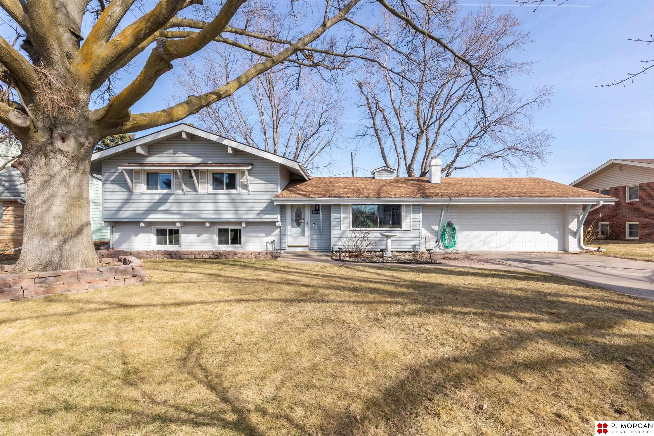 Gray split-level home with a two-car garage and a large leafless tree in the front yard.