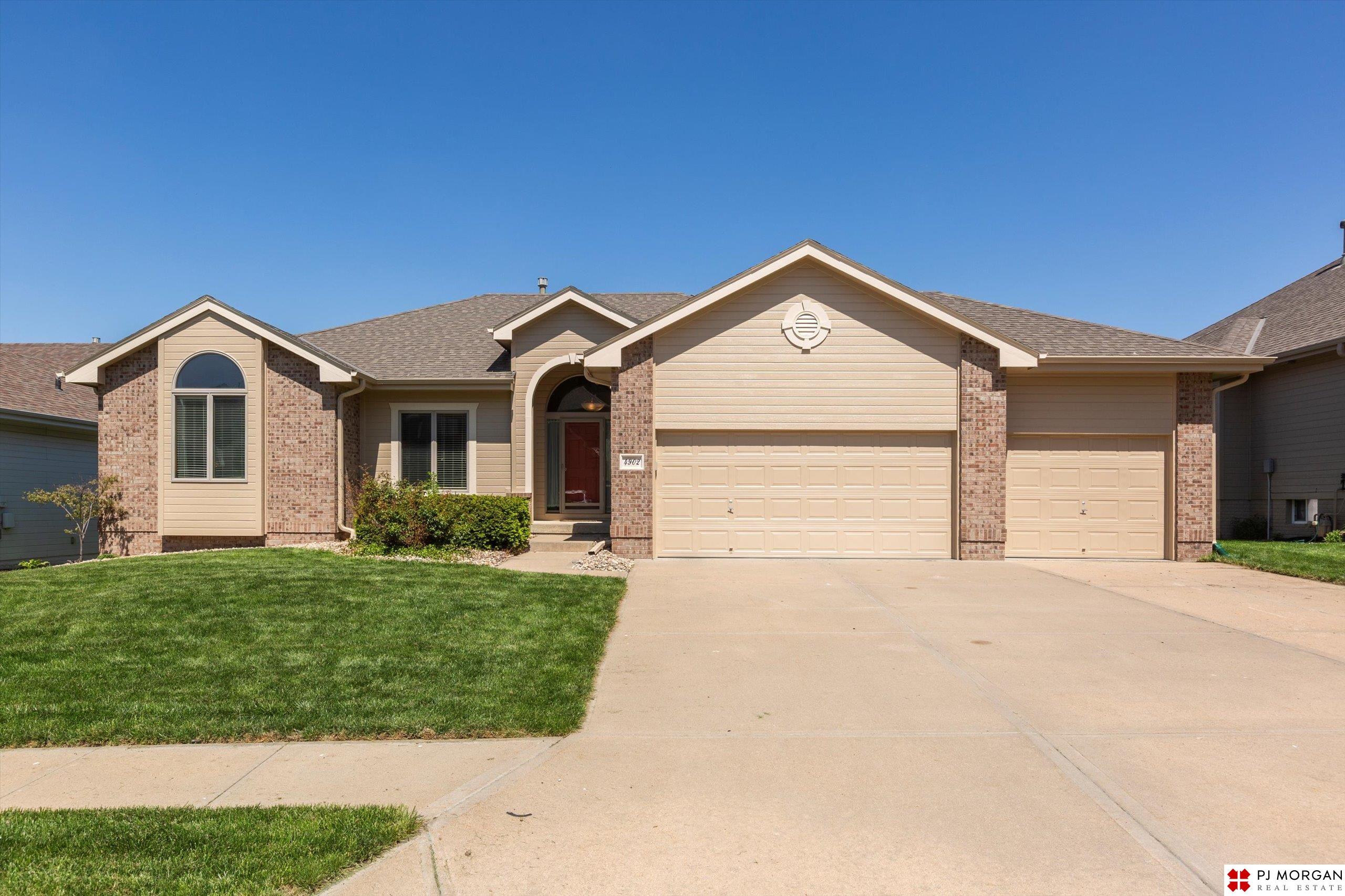 Tan and brick house with a three-car garage, arched entry, and broad concrete driveway.